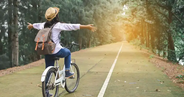 Ciclista en carretera forestal con brazos abiertos disfrutando vistas