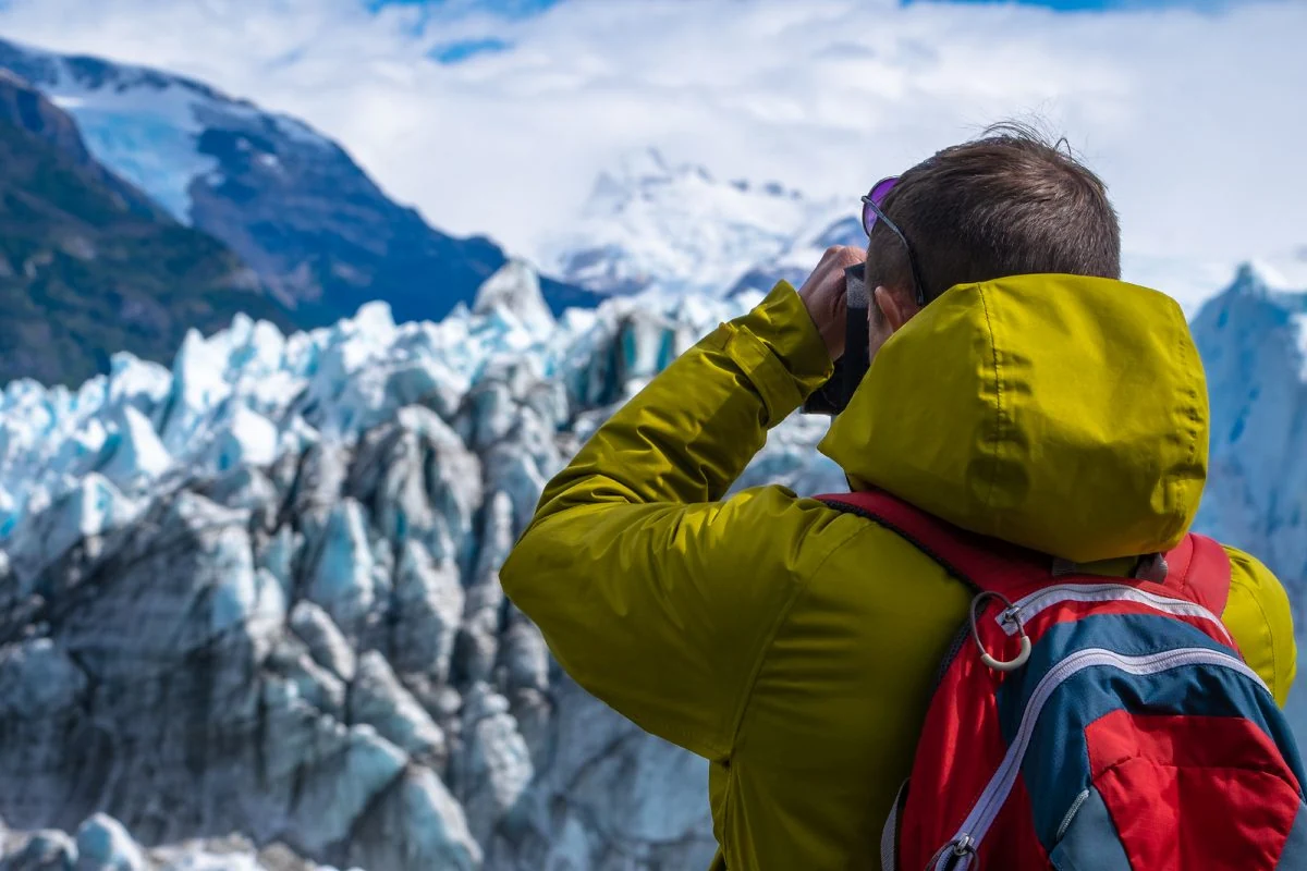 Fotógrafo con chaleco amarillo captura paisaje de montañas cubiertas de nieve