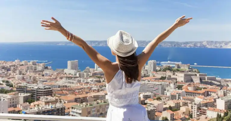 Mujer con brazos levantados en mirador con vista de costa mediterránea