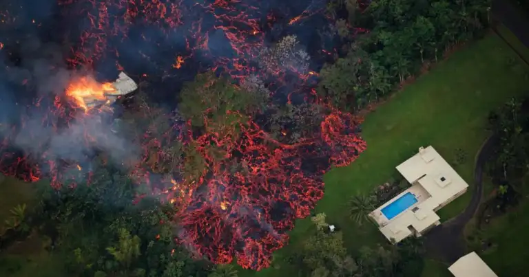 Vista aérea de volcán activo con flujo de lava roja y vivienda aislada