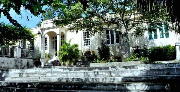 Casa blanca colonial con palmera y reja de hierro rodeada de árboles