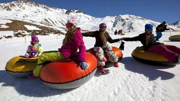 Niños en trineos inflables en nieve frente a montaña nevada