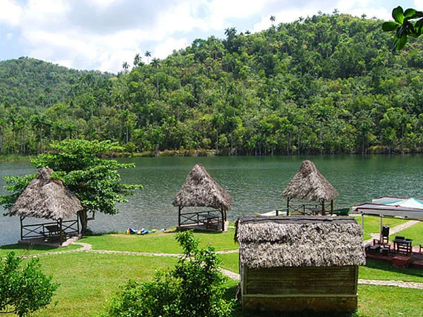 Cabañas con techo de paja y piscina natural junto a río tropical