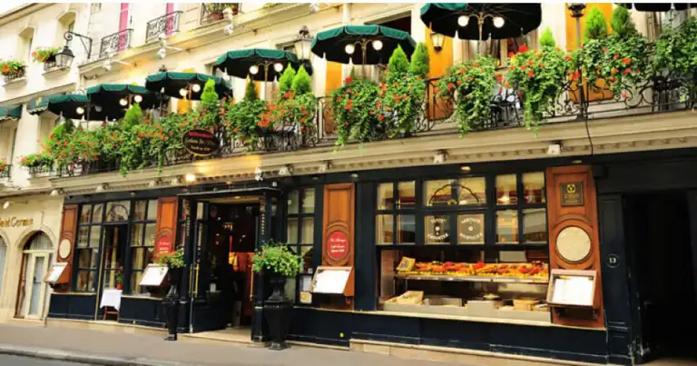 Fachada de café Le Procope en París con toldo negro, balcón y decoración floral