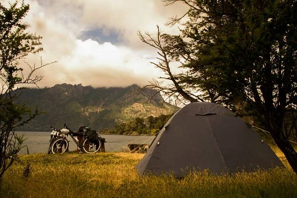 Tienda de campaña junto a lago montañoso con bicicleta aparcada