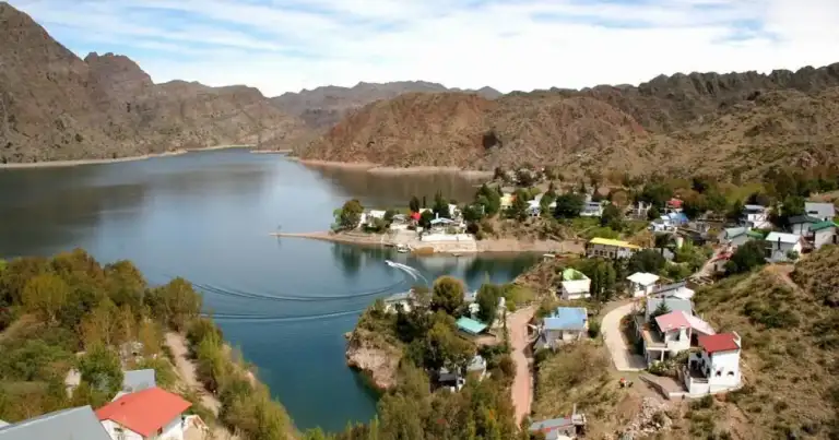 Embalse azul rodeado de montañas áridas con casas dispersas a la orilla