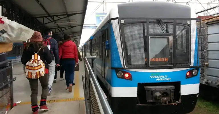 Tren de pasajeros en estación con viajeros en plataforma
