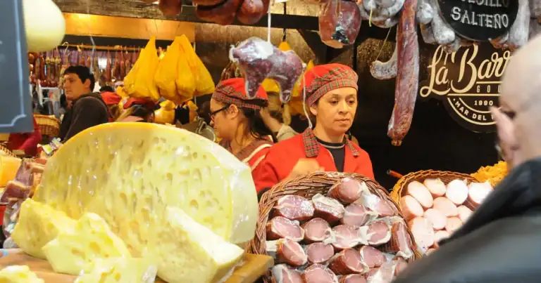 Puesto de feria con hortalizas, embutidos y vendedores en ropa colorida