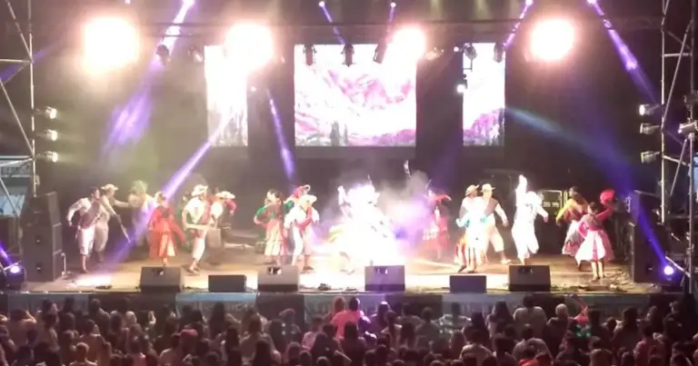 Artistas en traje tradicional actuando en escenario con iluminación ante público