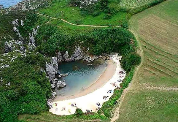 Playa semicircular de arena blanca rodeada de acantilados verdes