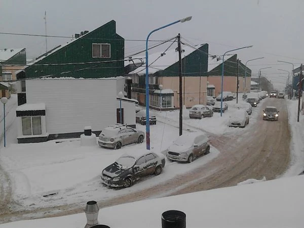 Calle de pueblo bajo nieve con casas y coches estacionados