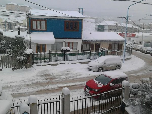 Casa bajo nieve con coche estacionado en calle nevada