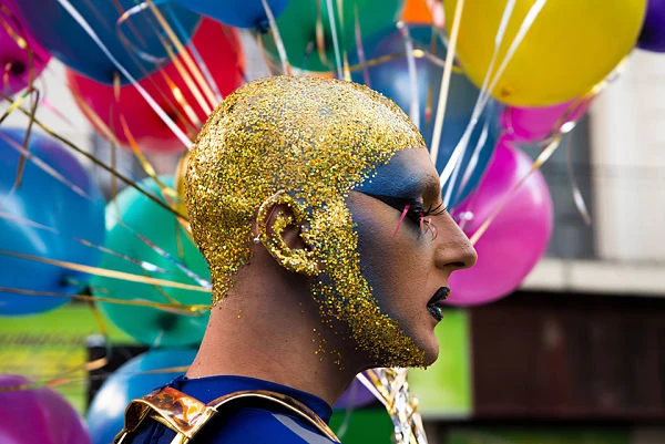 Persona con maquillaje dorado artístico y globos de colores de fondo