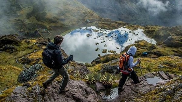 Trekistas en montaña alpina con lago rodeado de picos nevados