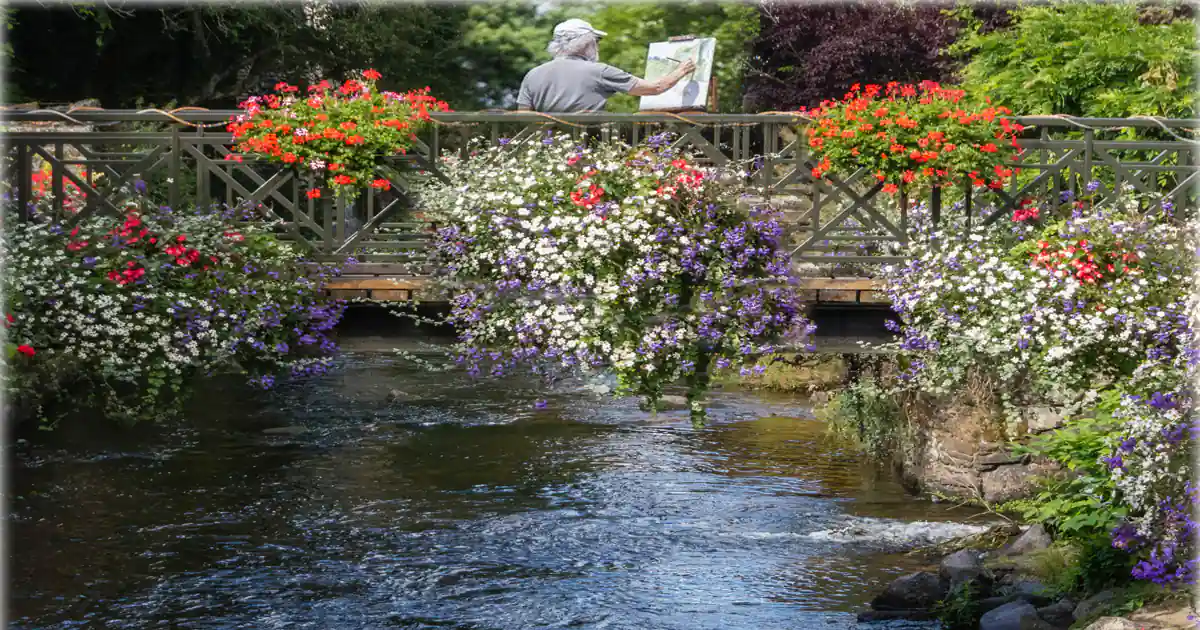 Puente de piedra sobre río con flores de colores en ambas orillas