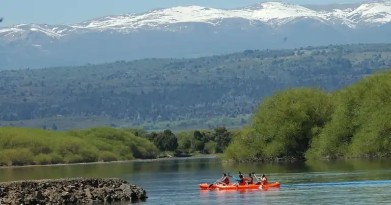 Río con montañas nevadas al fondo y grupo en bote rojo