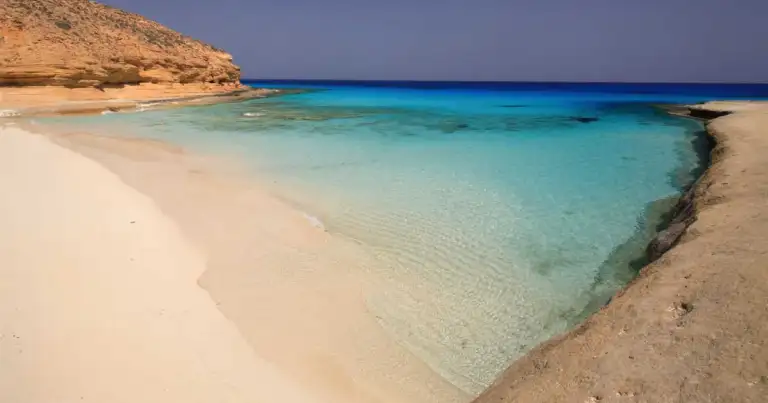 Playa de arena blanca y aguas turquesas frente a duna desértica