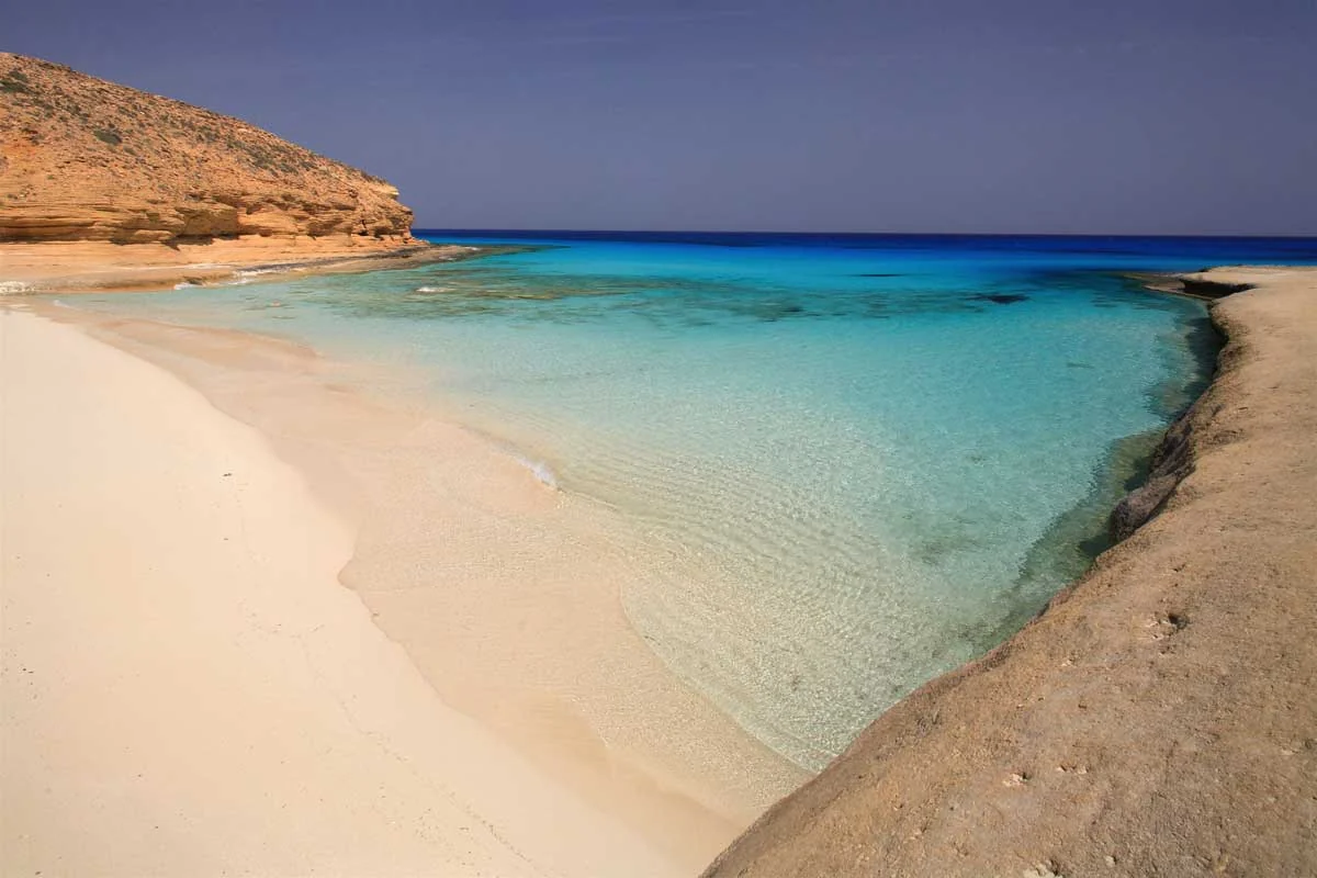 Playa de arena blanca y aguas turquesas frente a duna desértica