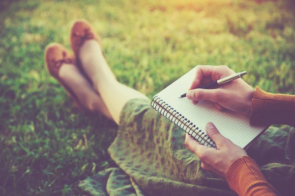 Persona escribe en cuaderno de espiral tumbada en hierba con botas
