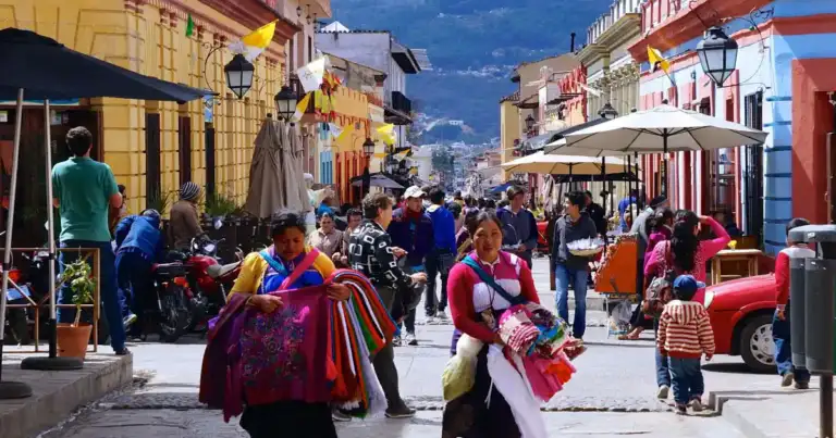 Calle colonial colorida con residentes en ropa tradicional y montañas