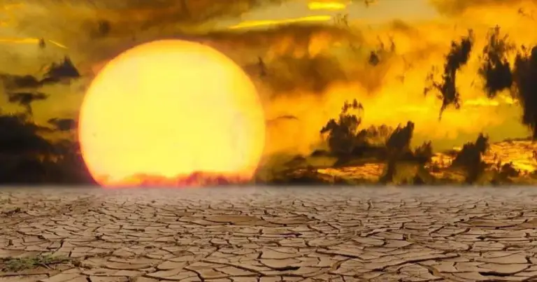 Sol gigante en puesta sobre tierra árida y resquebrajada