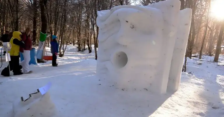 Escultura de hielo blanca en parque nevado con visitantes alrededor