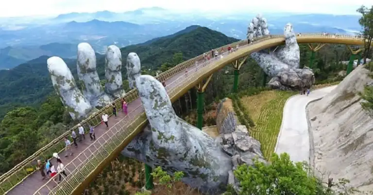 Puente arqueado dorado soportado por manos gigantes sobre paisaje boscoso