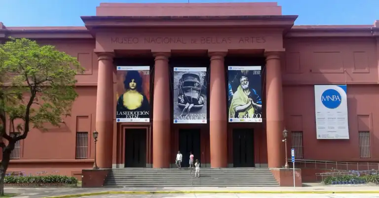 Fachada de museo histórico rojo con columnas, escalinata y banderas