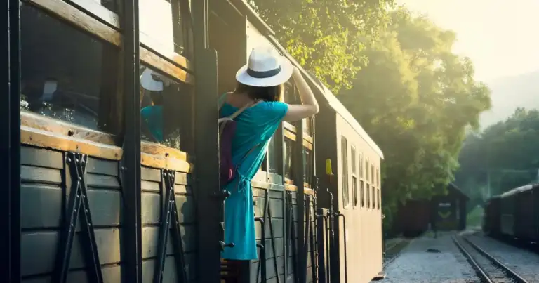 una mujer con sombrero mira desde el escalon de un tren en marcha