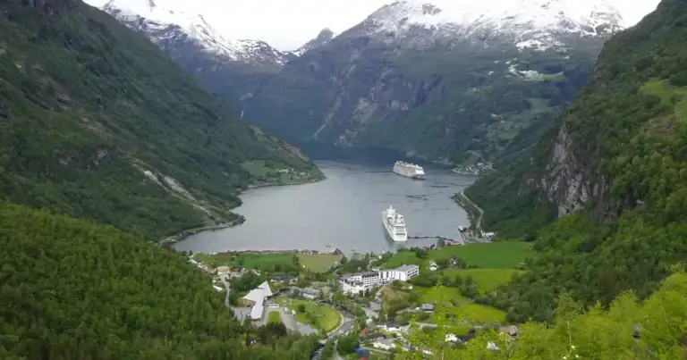 Vista del pueblo de Geiranger y del fiordo desde lo alto, con cruceros anclados entre montañas nevadas