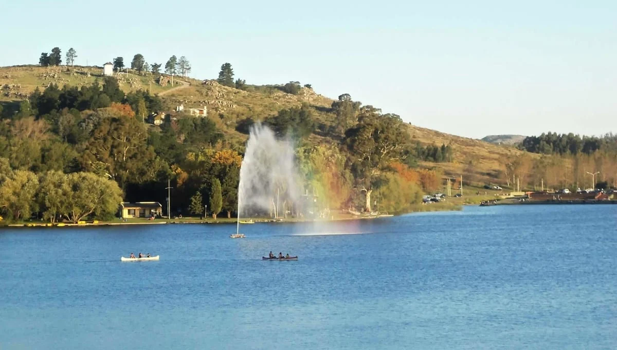 Lago rodeado de montañas verdes con fuente de agua alta y botes