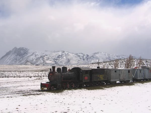Tren antiguo de vapor en la nieve con montañas nevadas de fondo