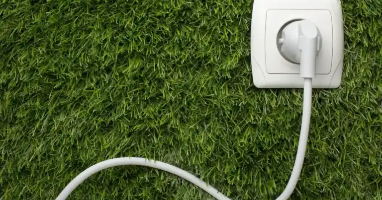 Cable eléctrico blanco conectado a enchufe sobre césped verde