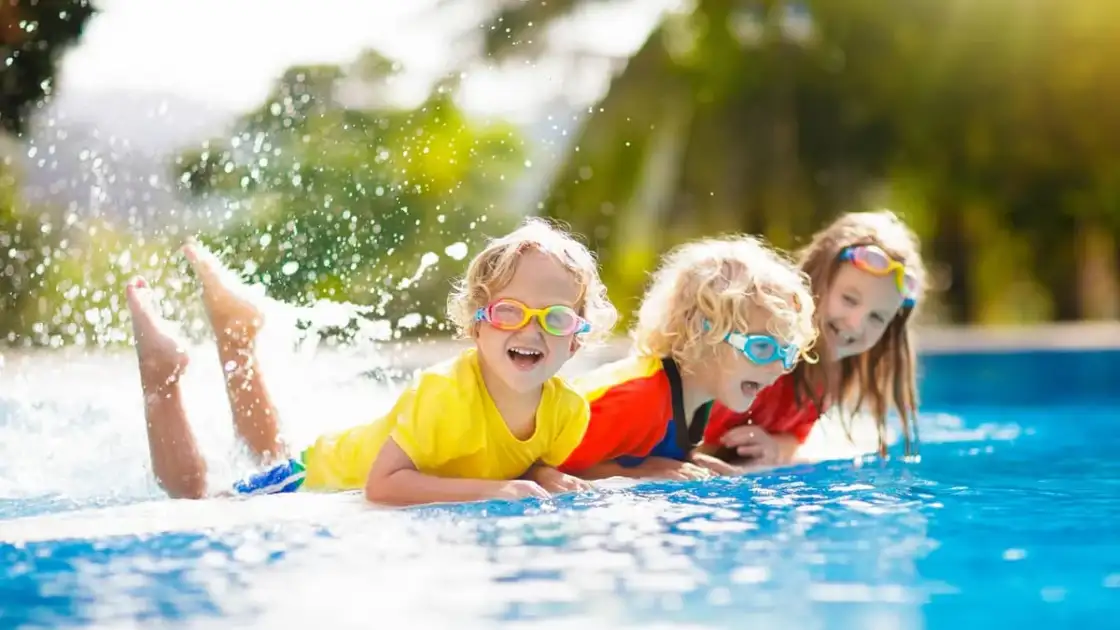 Tres menores jugando en piscina azul con agua salpicada