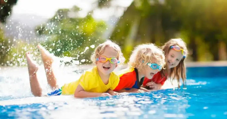 Tres menores jugando en piscina azul con agua salpicada