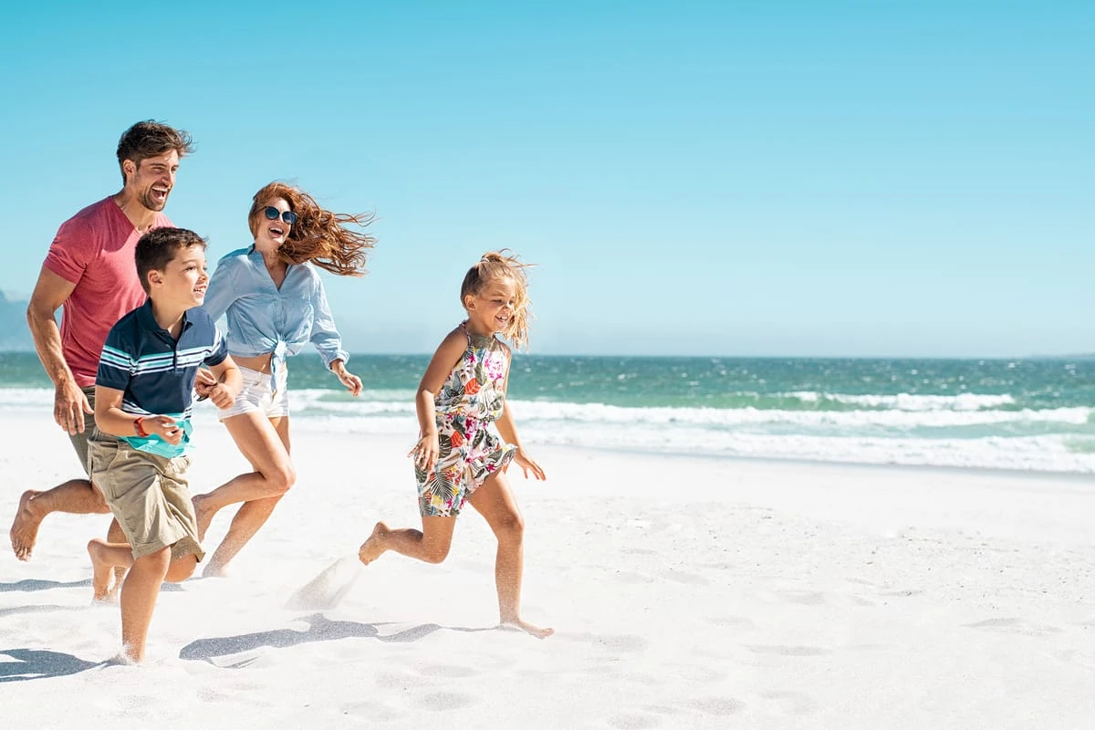 Familia con niños corriendo y jugando en playa arenosa junto al mar