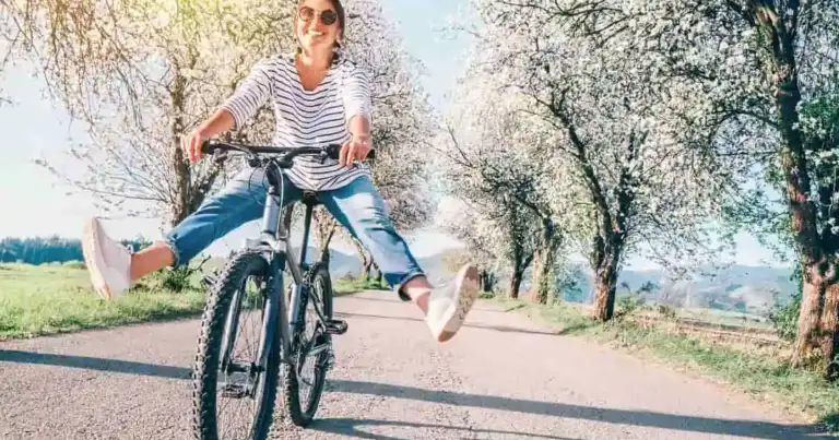 mujer en bicileta en un camino lleno de arboles en flor