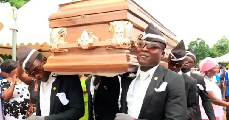 Hombres en traje formal y sombrero llevando ataúd marrón en procesión