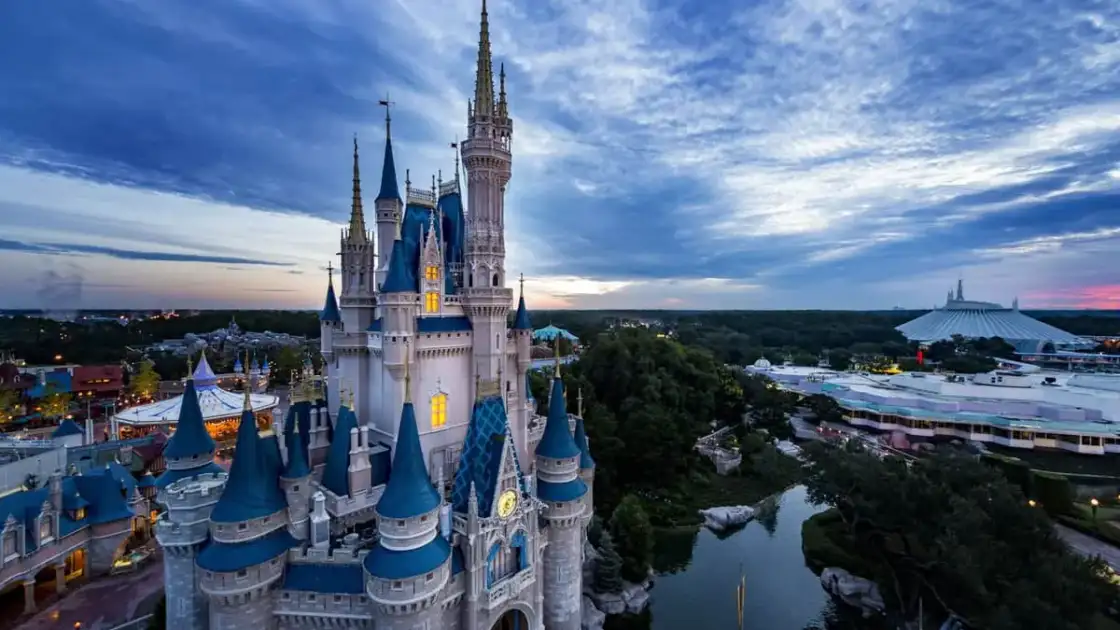 Castillo de Disney con torres puntiagudas iluminado al atardecer, rodeado del parque temático