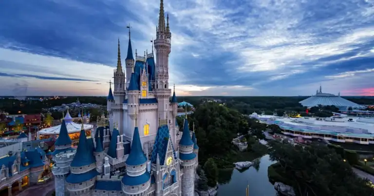 Castillo de Disney con torres puntiagudas iluminado al atardecer, rodeado del parque temático