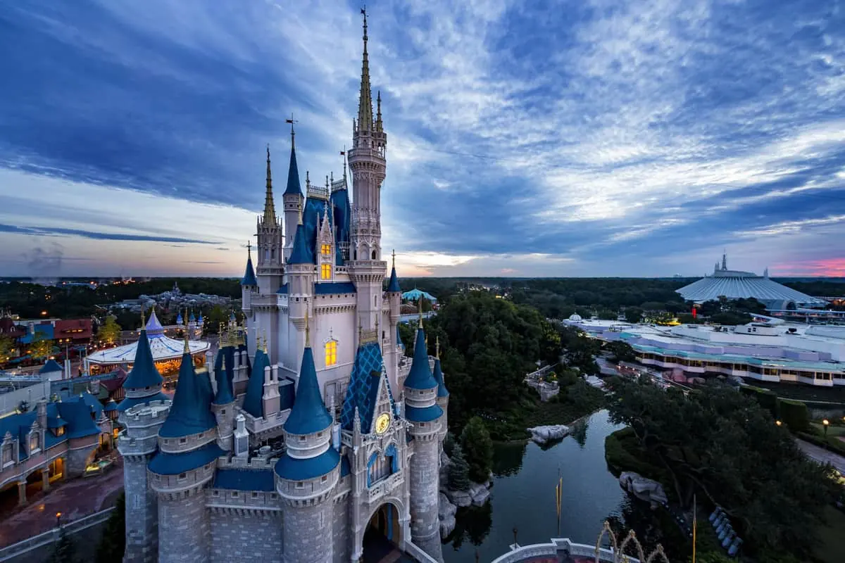 Castillo de Disney con torres puntiagudas iluminado al atardecer, rodeado del parque temático
