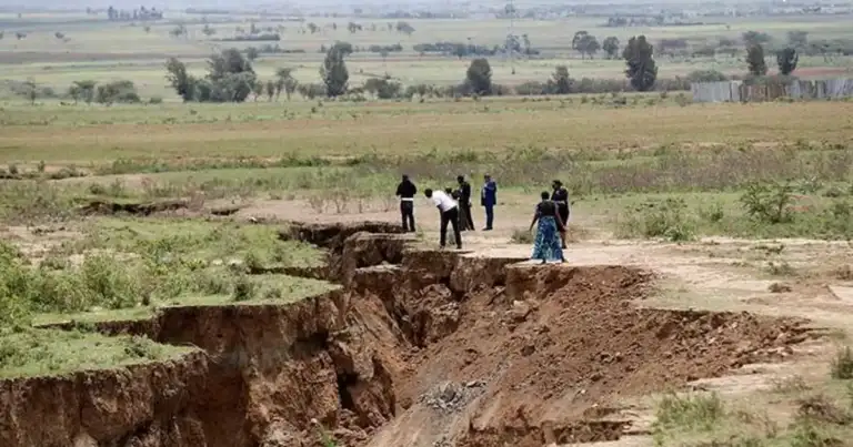 Grieta profunda en terreno árido con grupo de personas observando desde el borde