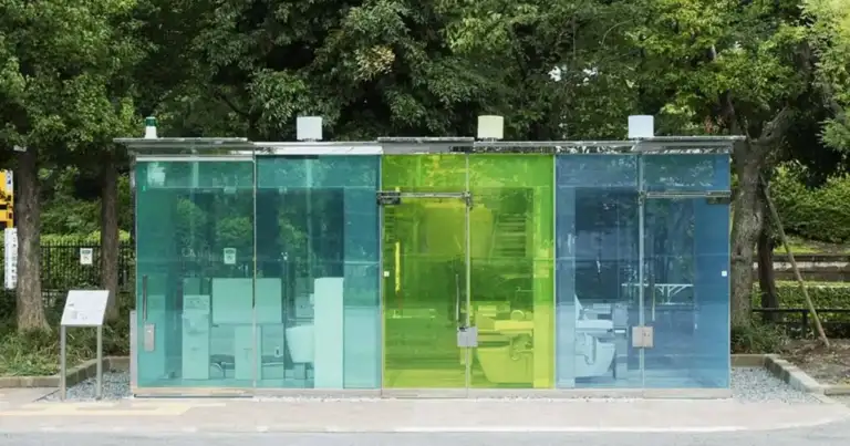 Baños públicos construidos con paneles de cristal transparente en tonos verde y azul