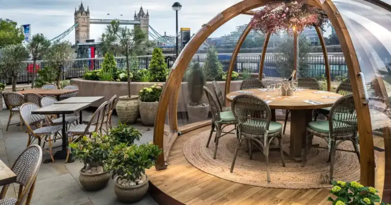 Restaurante con estructura de iglú transparente junto a puente sobre río urbano
