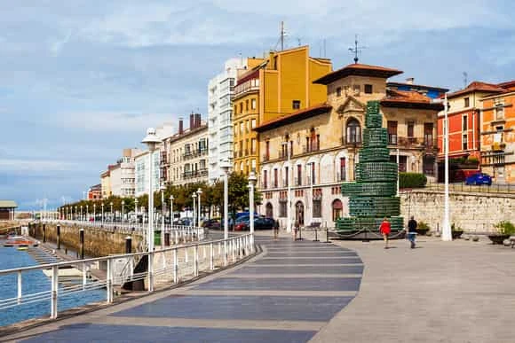 Paseo marítimo costero con edificios de arquitectura colorida y barcos en puerto