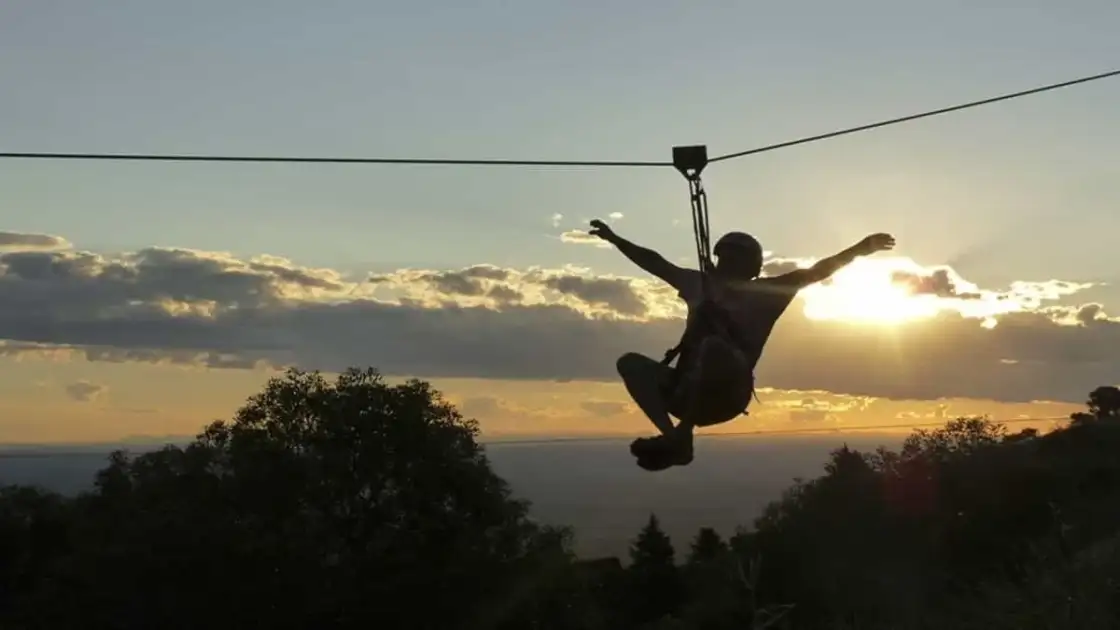 Persona practicando tirolesa al atardecer en Merlo, San Luis, con sierras y cielo dorado de fondo