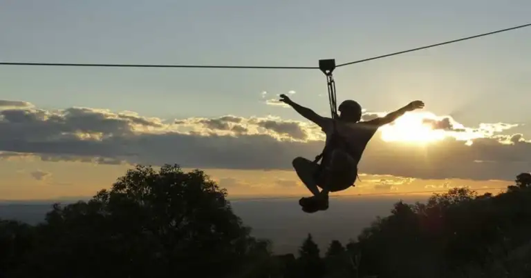 Persona practicando tirolesa al atardecer en Merlo, San Luis, con sierras y cielo dorado de fondo