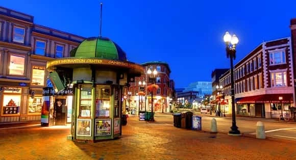 Plaza comercial nocturna con negocios iluminados y arquitectura histórica
