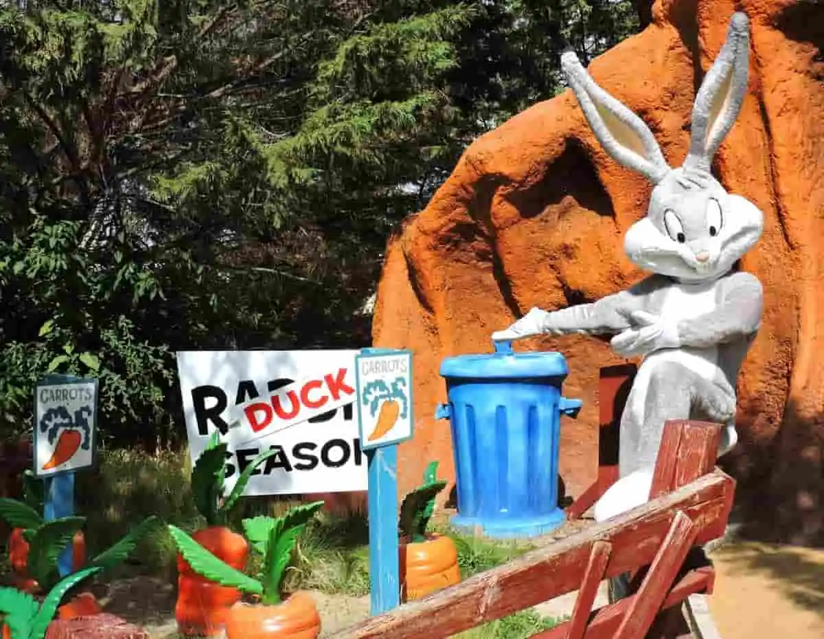 Personaje disfrazado de conejo blanco junto a cartel y decoraciones de parque