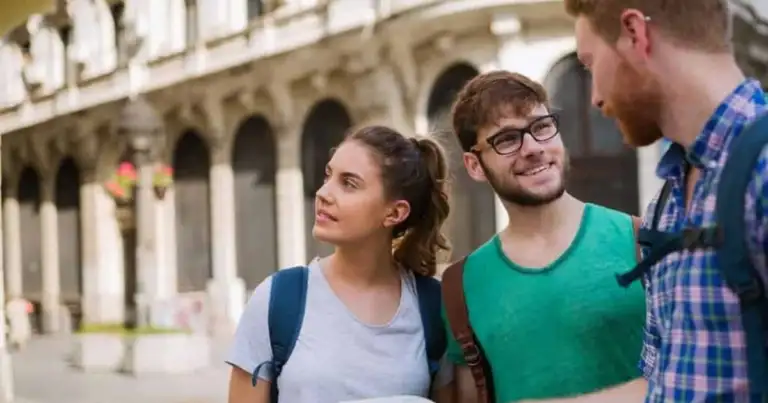 Grupo de tres turistas jóvenes en plaza con columnata y arquitectura de arcadas al fondo